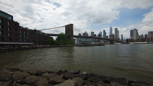 Bridge over river by buildings in city against sky