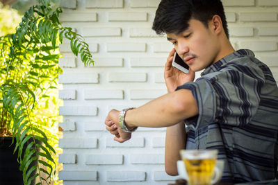 Young man using mobile phone against wall