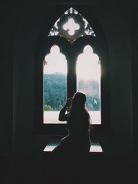 Silhouette woman looking through window in building