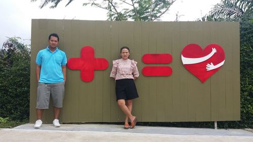 Portrait of couple standing against wall with sings and heart shape