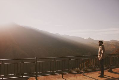 Side view of man standing by railing against sky