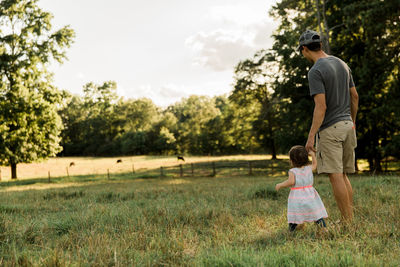 Father and daughter standing on field against sky