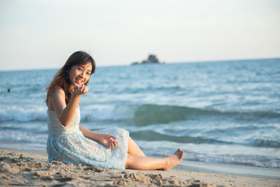 Young woman sitting on shore at beach against sky