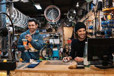 Positive young male technician assembling bike while colleague working on computer in professional workshop