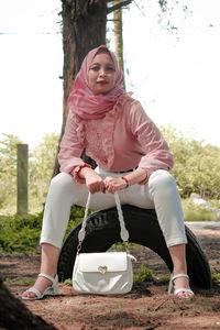 Full length portrait of young woman sitting outdoors