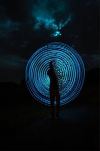 Silhouette man standing by illuminated light against sky at night