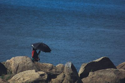 High angle view of woman with umbrella standing at rocky beach