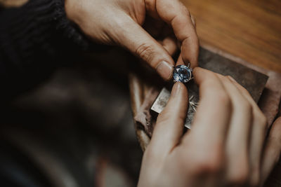 Unrecognizable goldsmith holding gem and metal ornament over table while making ring in workshop