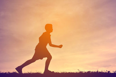 Silhouette boy running on field against sky during sunset