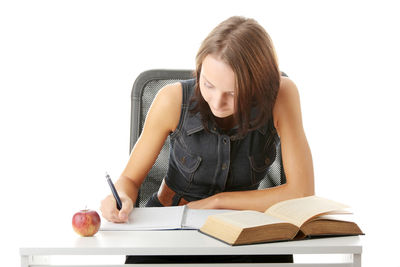 Young woman sitting on book against white background
