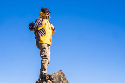 Low angle view of man standing on rock against blue sky