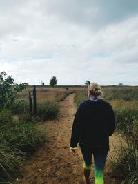 Rear view of woman walking on field against sky