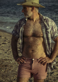 Adult man in cowboy hat with open shirt on beach against sea