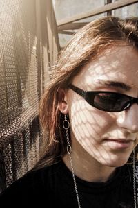 Close-up of young woman wearing sunglasses against fence