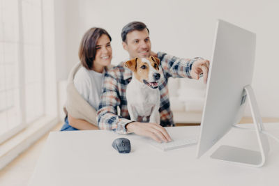 Smiling couple with dog using computer on table at home