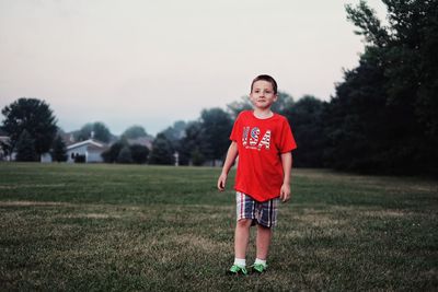 Smiling boy standing on grassy field at park against clear sky