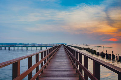 Diminishing perspective of pier over sea against sky during sunset