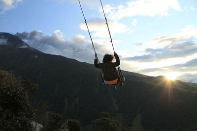 Woman swinging on mountain against sky