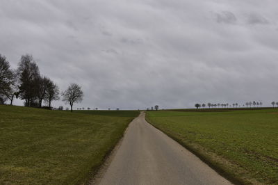 Empty road amidst field against sky