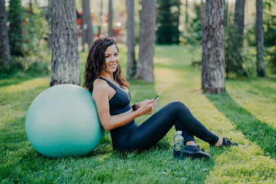 Woman with smart phone sitting by fitness ball in park