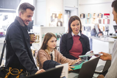 Sales clerk showing computer equipment to family in electronics store