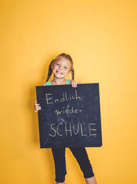 Portrait of smiling girl standing against yellow background