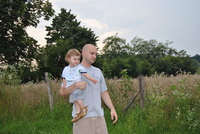 Bald father carrying cute son while standing on field