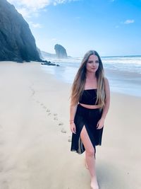 Young woman standing at beach against sky