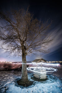 Bare tree by frozen lake against sky during winter