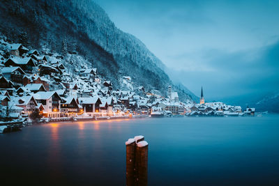 Sea by illuminated buildings against sky at dusk