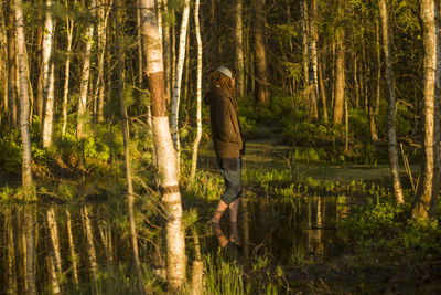 Side view of woman standing in lake against trees at forest