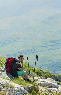 Side view of hiker sitting on rocks by landscape