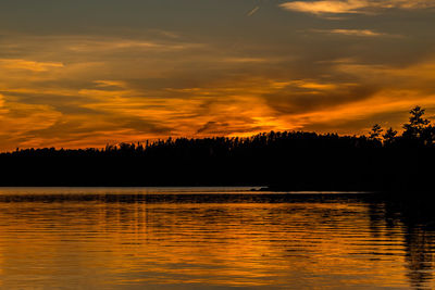 Silhouette trees by river against orange sky during sunset