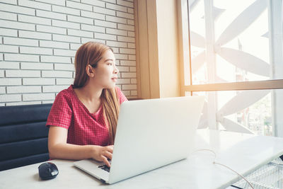 Young businesswoman looking away while using laptop at table in cafe