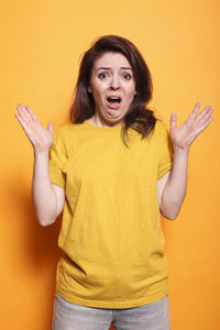 Portrait of young woman with arms crossed standing against yellow background