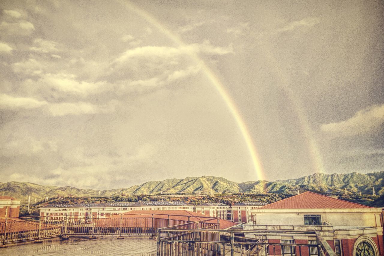 rainbow, mountain, sky, built structure, railing, building exterior, water, architecture, cloud, mountain range, pier, cloud - sky, multi colored, scenics, day, beauty in nature, outdoors, atmospheric mood, nature, tranquility, majestic, tranquil scene, no people, atmosphere