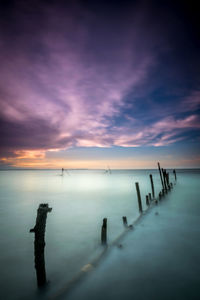 Wooden posts in sea against sky during sunset