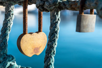 Close-up of a rusty heart-shaped padlock, with an out-of-focus sea background.