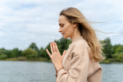 Caucasian woman sitting in a lotus position and holding hands in a namaste gesture