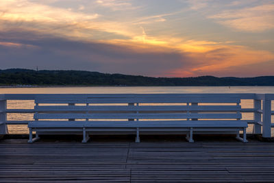 Empty bench by sea against sky during sunset