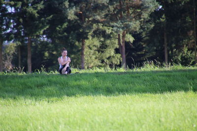 Young woman sitting on grassy field during sunny day