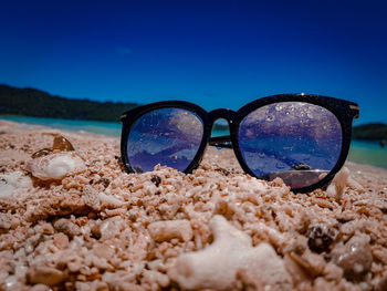 Close-up of sunglasses on beach against clear blue sky