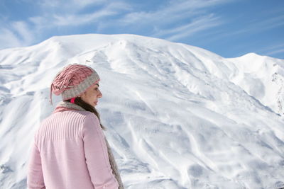 Woman in pink sweater standing against snow covered mountain against sky