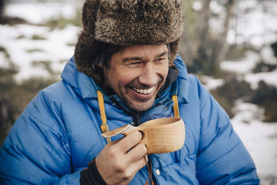 Happy mature man in warm clothing drinking tea in wooden cup