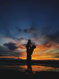 Silhouette woman standing at beach against sky during sunset