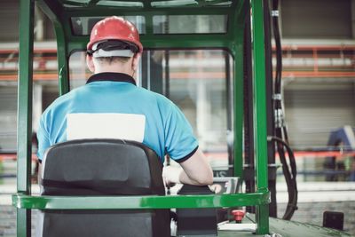 Rear view of man sitting in forklift in factory