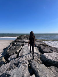 Rear view of woman standing on rock by sea against sky