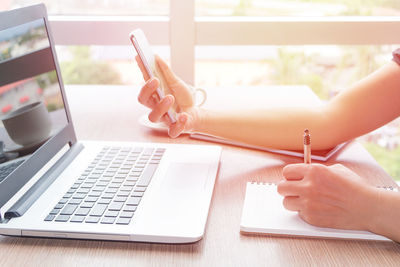 Cropped hands of businesswoman using technologies at desk in office