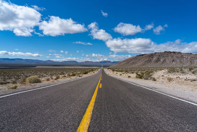 Road leading towards mountains against blue sky