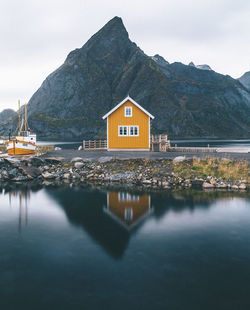 House by lake and mountains against sky